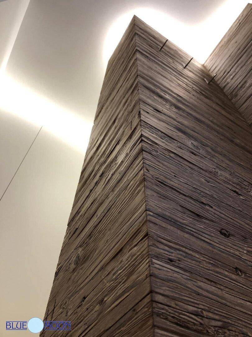 Rustikale Holzsäule mit strukturierter Oberfläche, beleuchtet von indirektem Licht.