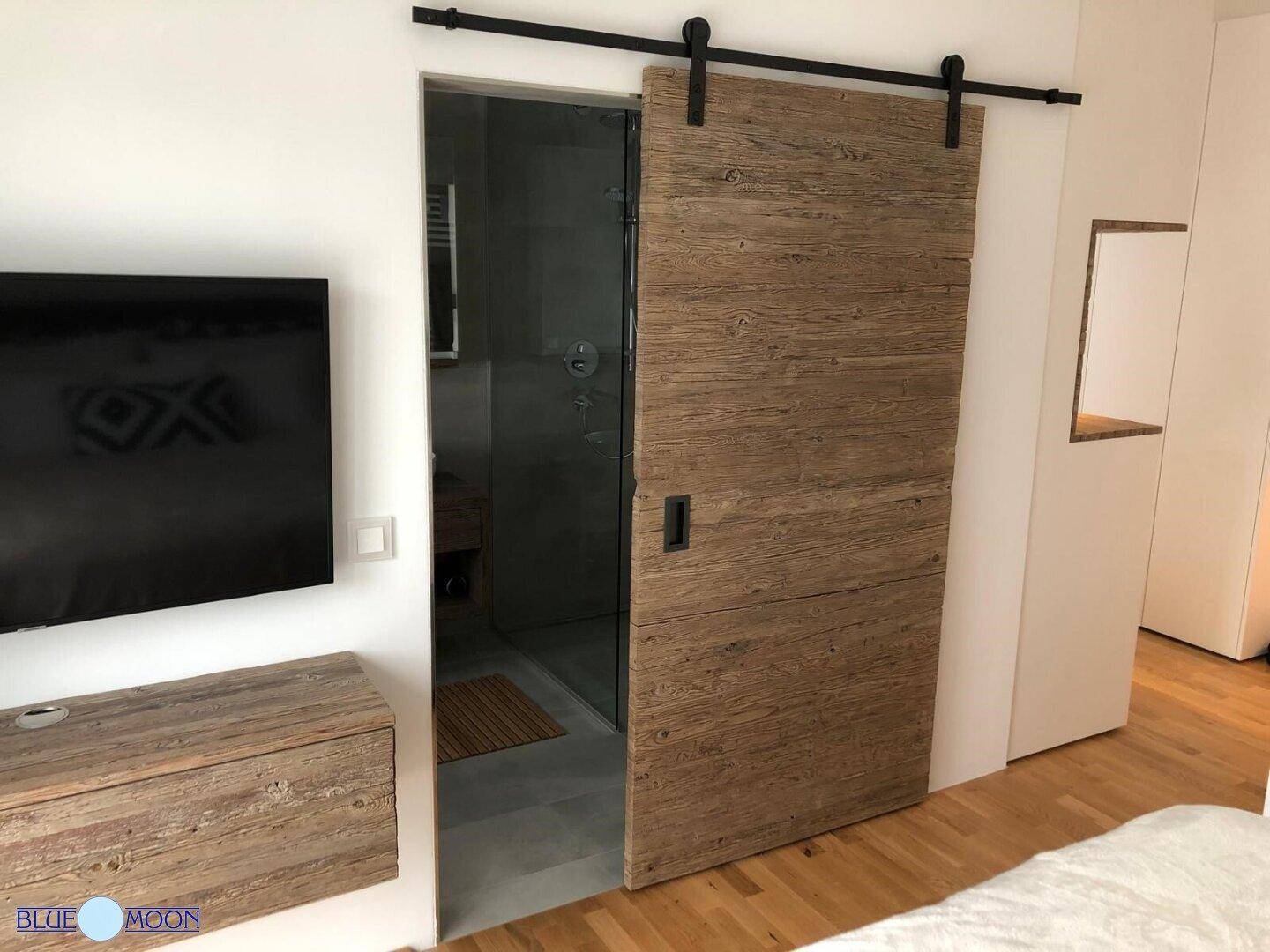 Schlafzimmer mit Holzboden und moderner Schiebetür, die zum Badezimmer führt.