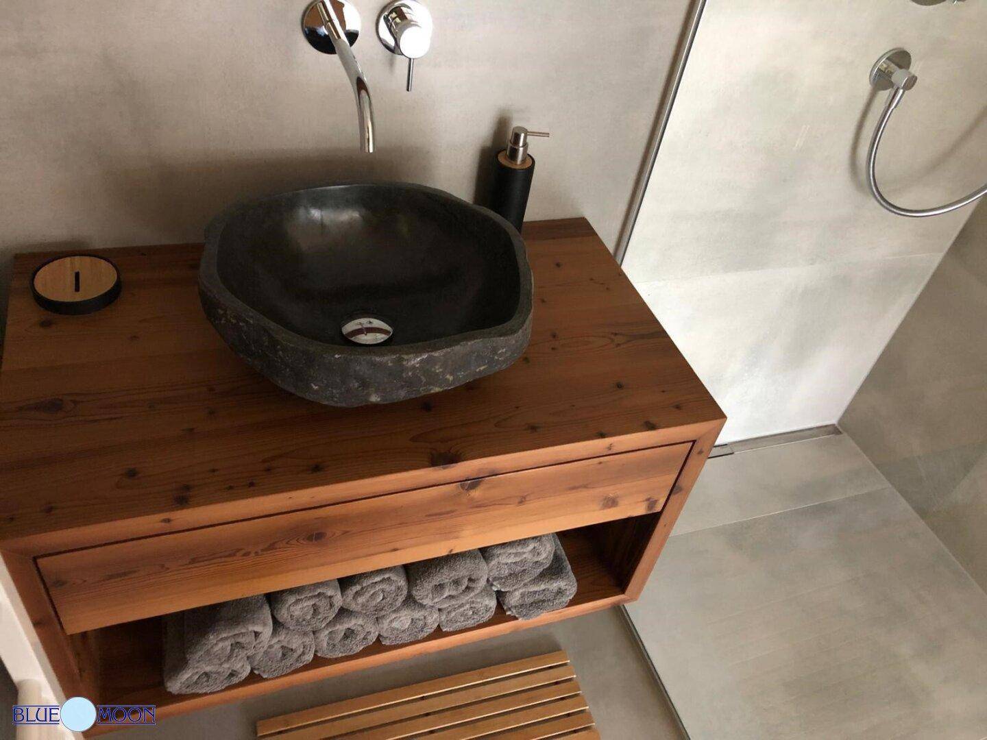 Rustikaler Waschtisch aus Holz mit einem einzigartigen Steinwaschbecken und modernen Armaturen.