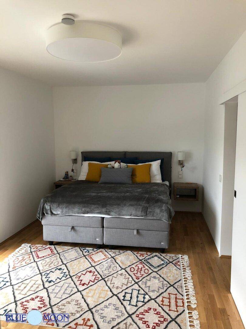 Helles Schlafzimmer mit Doppelbett, Holzboden und farbenfrohem Teppich.