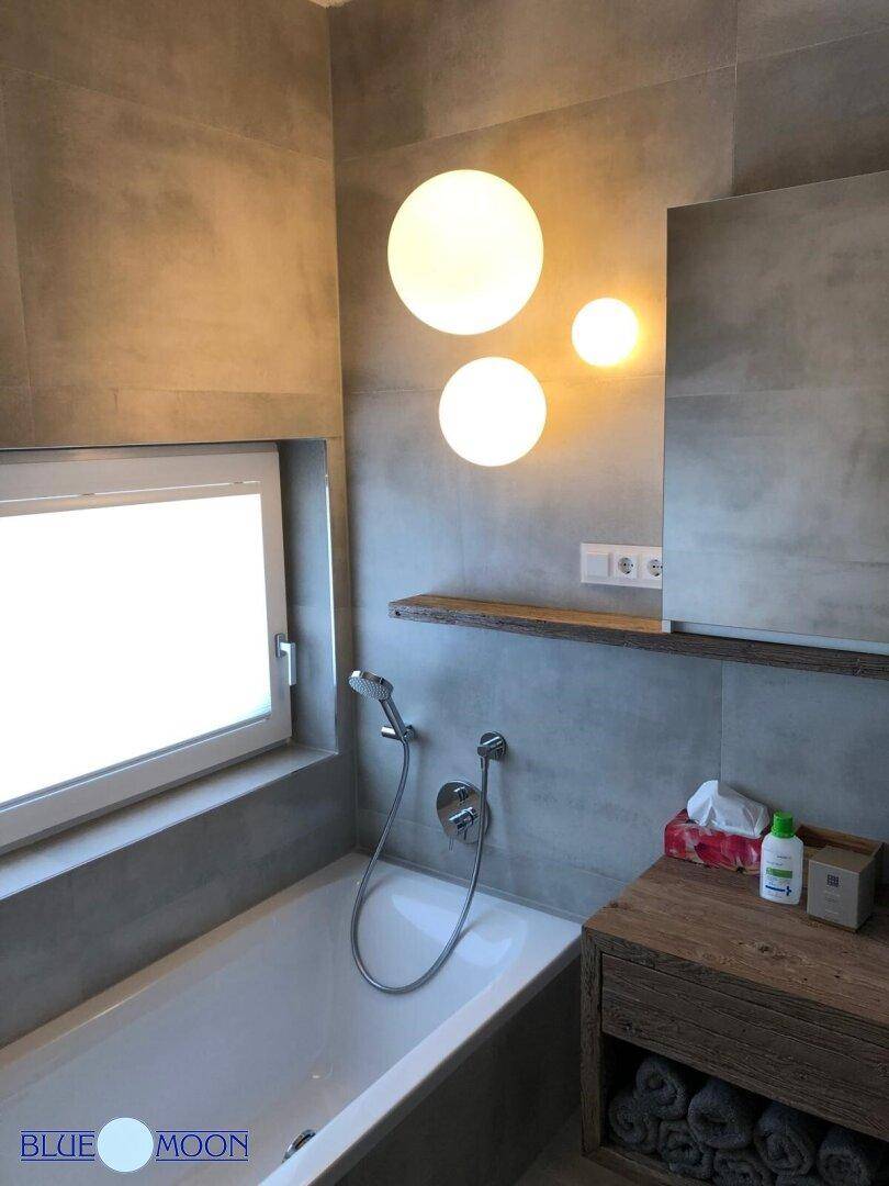 Modernes Badezimmer mit Badewanne, Fenster und grauen Fliesen.