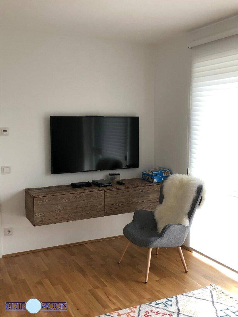 Wohnbereich mit Wandfernseher, schwebendem Sideboard und bequemen Sessel.