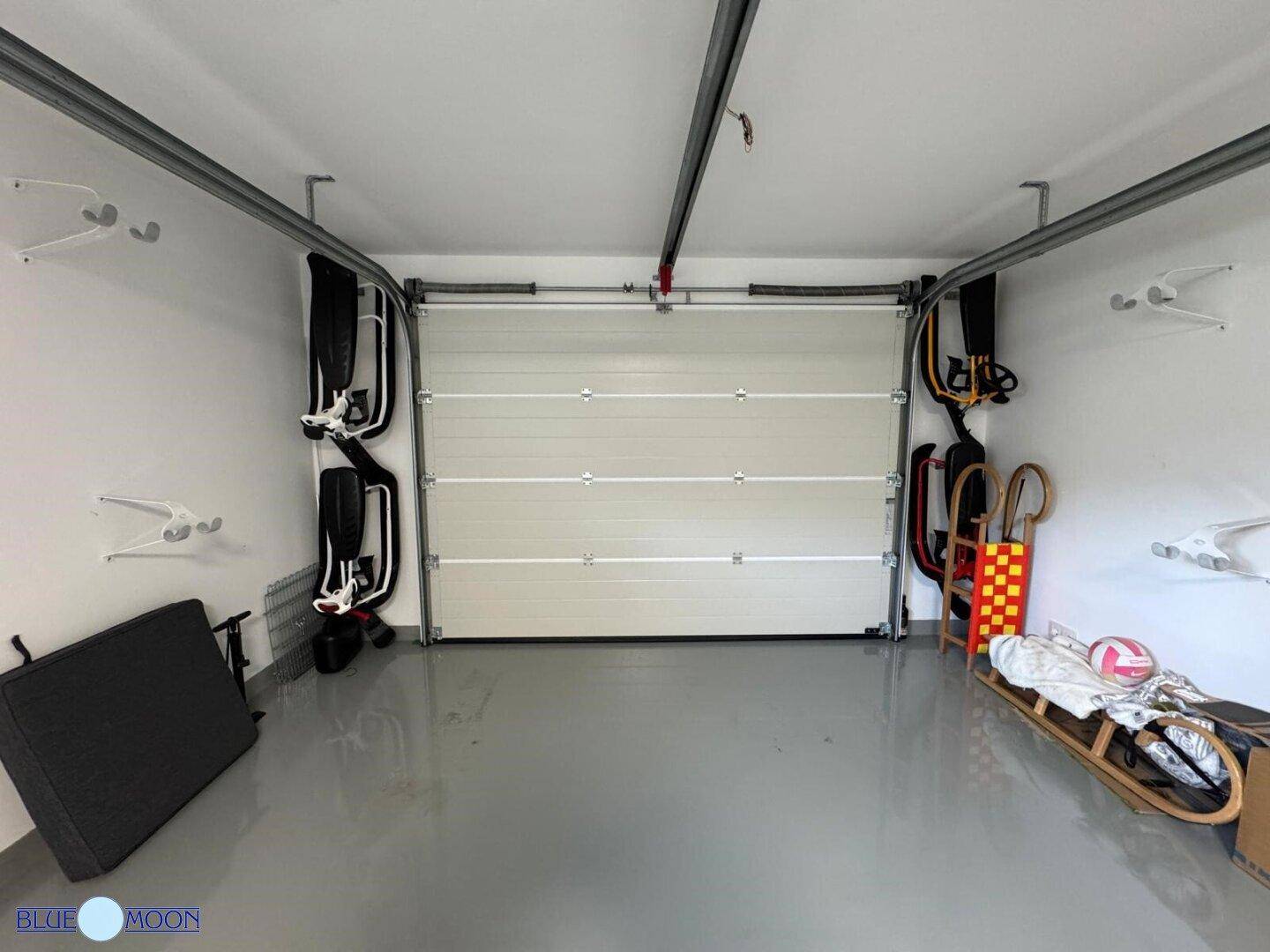 Innenansicht der Garage mit geschlossenem Tor und Stauraum für Sportgeräte und Polster.
