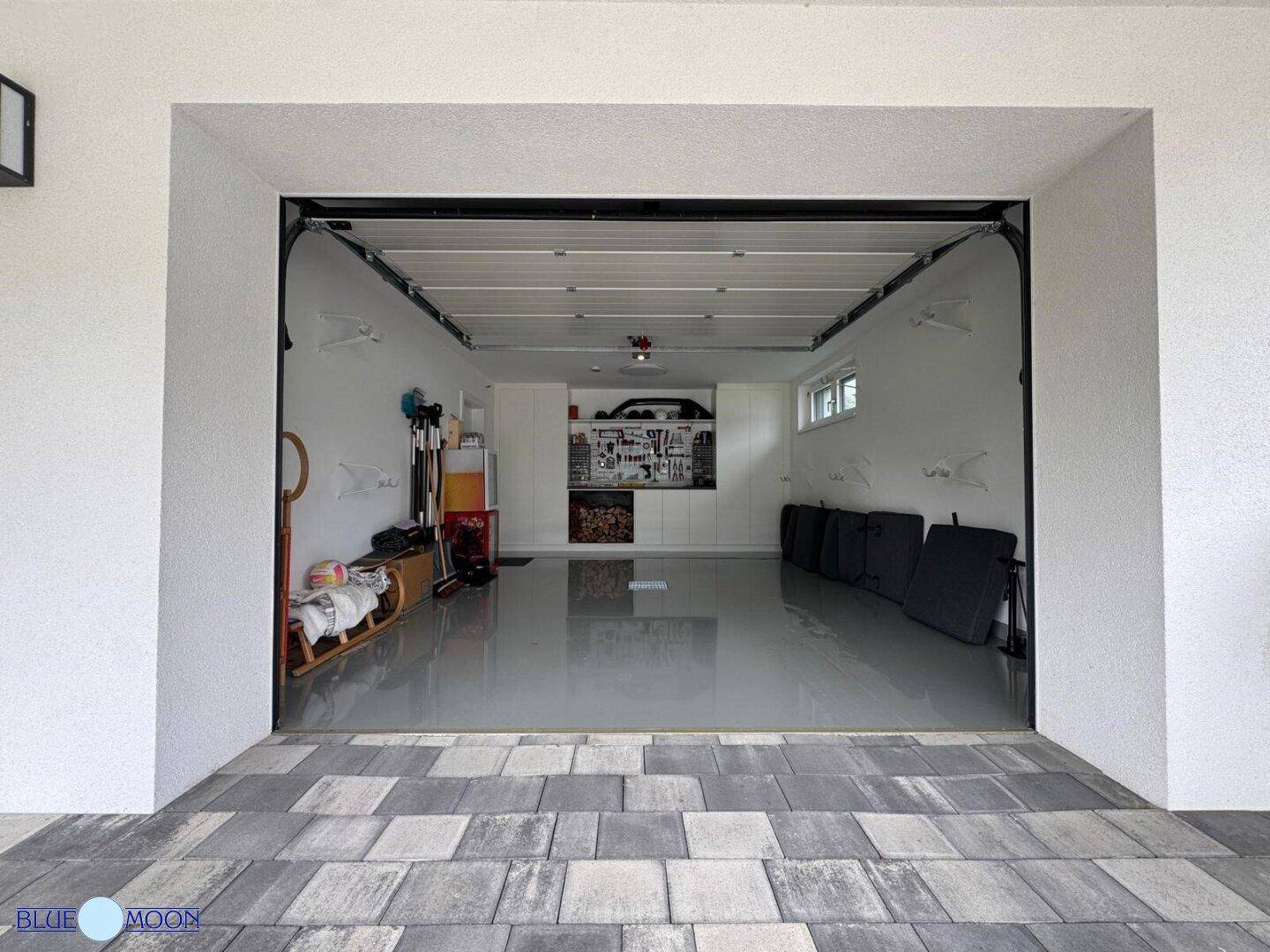 Geräumige Garage mit Werkstattbereich und Blick auf die gepflasterte Einfahrt und das Grundstück.