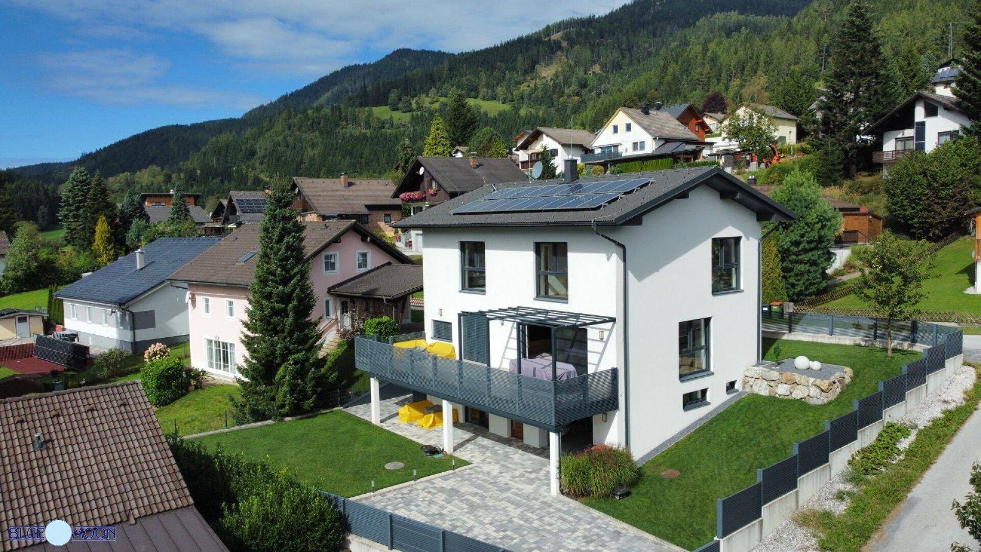 Modernes Einfamilienhaus mit Balkon, Solaranlage und Bergblick in grüner Umgebung.