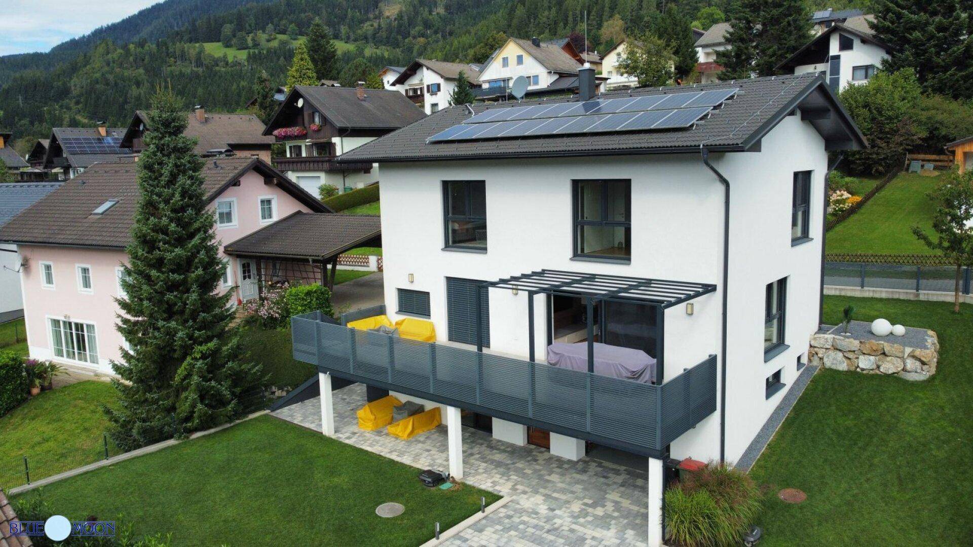 Modernes Einfamilienhaus mit Balkon, Solaranlage und gepflegtem Garten in den Bergen.