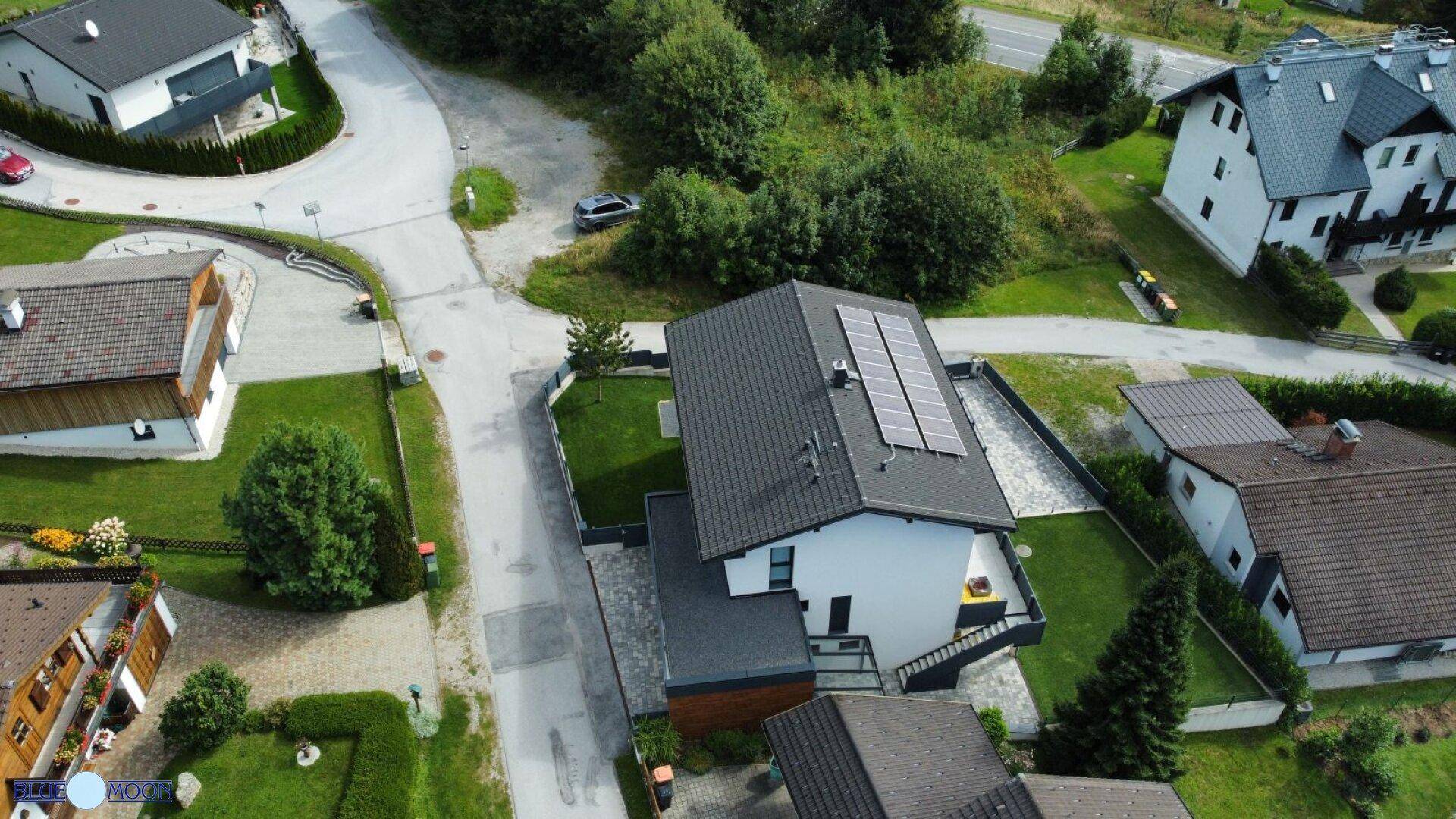 Luftaufnahme eines modernen Hauses mit Solaranlage auf dem Dach und umliegender Landschaft.