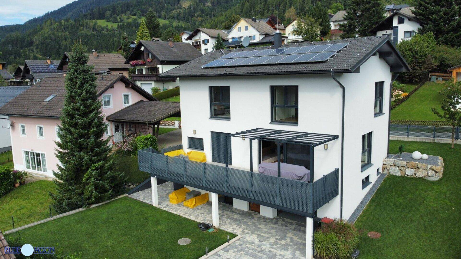 Modernes Einfamilienhaus mit Balkon, Solaranlage und gepflegtem Garten in den Bergen.