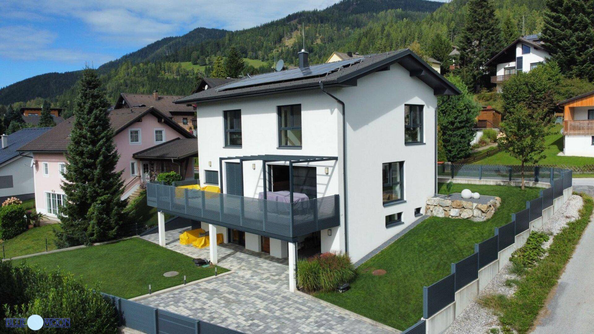 Modernes Einfamilienhaus mit Balkon, Solaranlage und gepflegtem Garten in den Bergen.