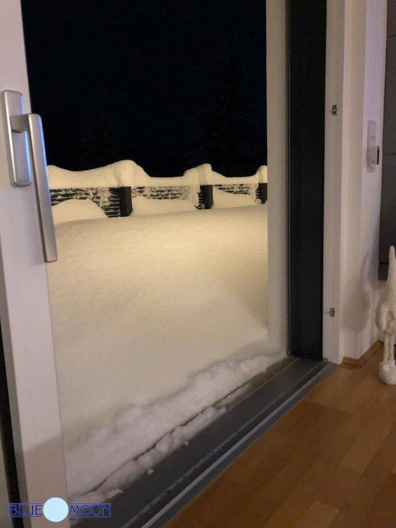 Blick aus dem Fenster auf den verschneiten Gartenbereich bei Nacht mit hohem Schnee.