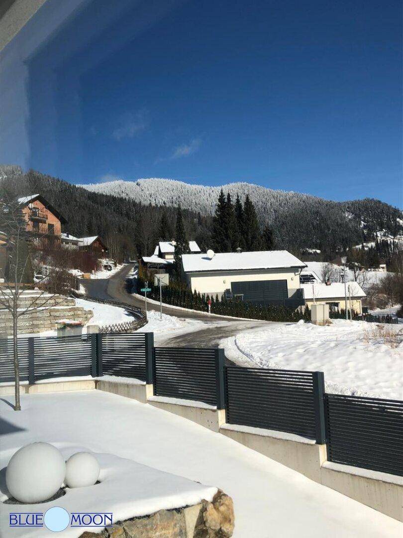 Winterlandschaft mit verschneitem Garten und Bergblick unter blauem Himmel an einem sonnigen Tag.