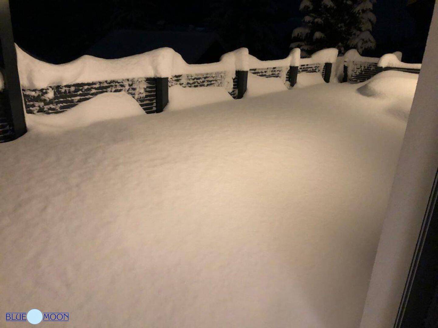 Verschneiter Gartenbereich bei Nacht, bedeckt mit einer dicken Schneedecke und Zaun.