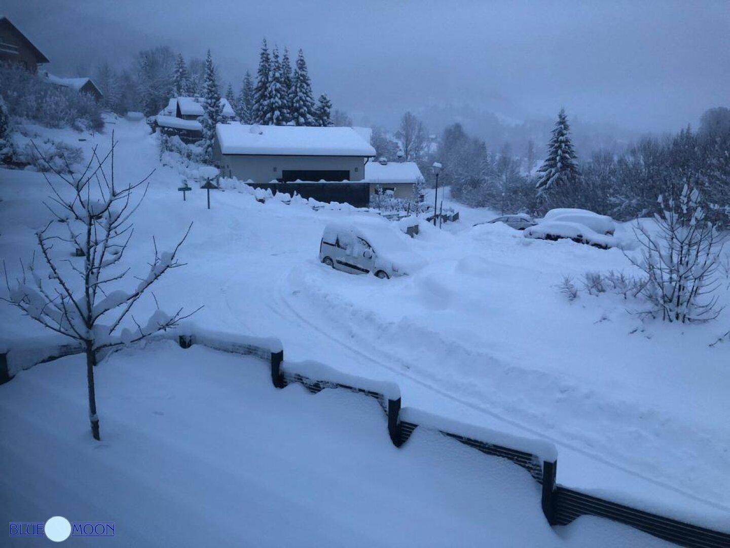 Verschneite Winterlandschaft mit Häusern und einem Auto im Schnee in den Bergen.