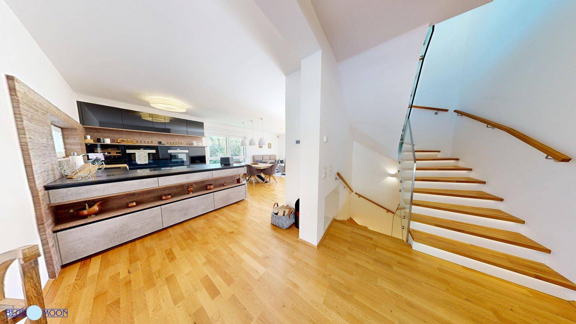 Offener Wohn- und Essbereich mit moderner Küche, Holzboden und Treppe.