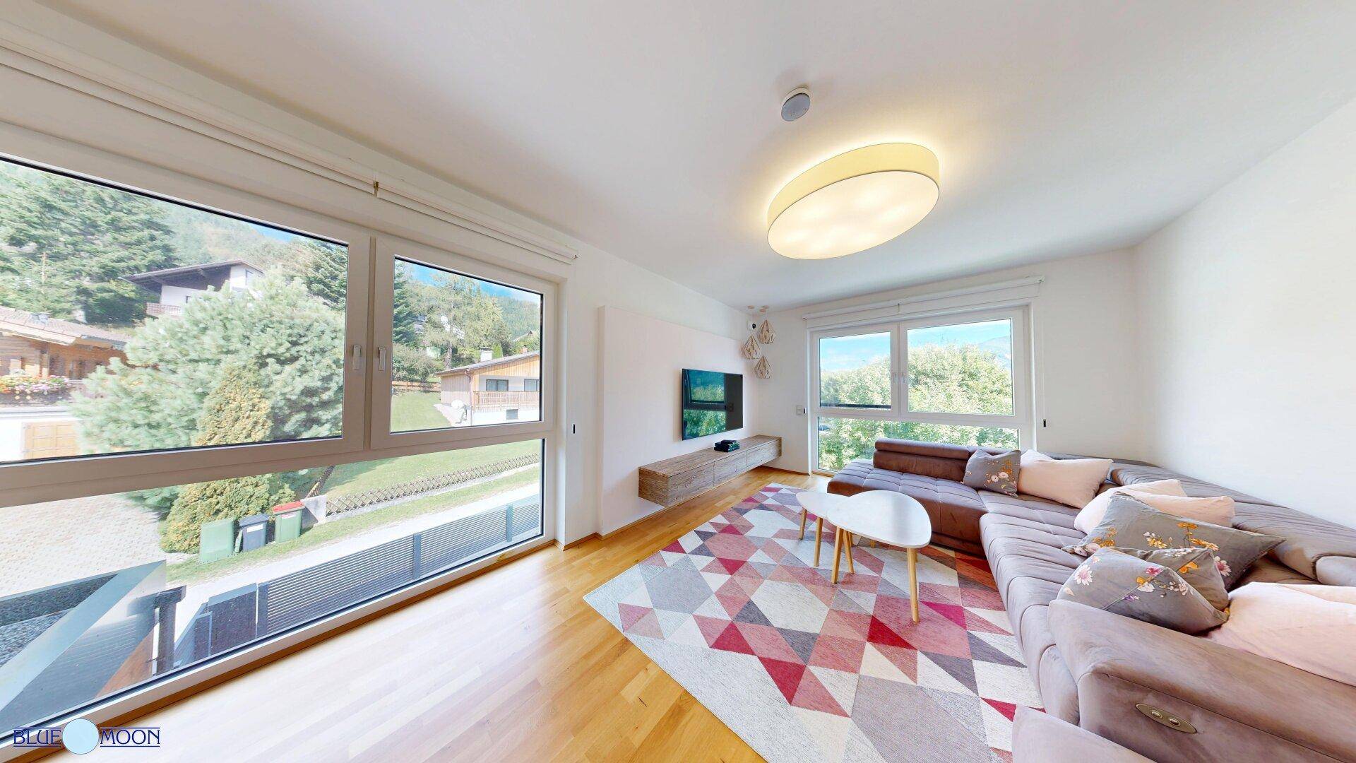 Helles Wohnzimmer mit großem Sofa, Holzboden und weitem Blick ins Grüne.