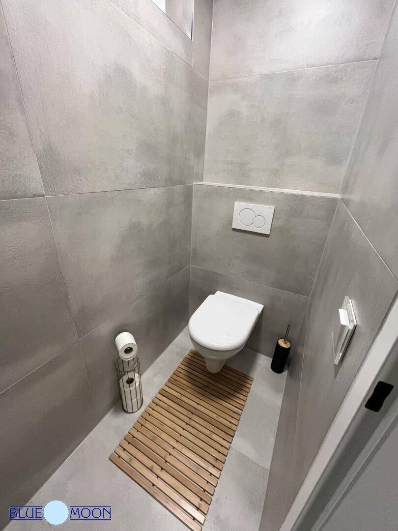 Modernes Gäste-WC mit Wand-WC und grauen Fliesen an Wänden und Boden.