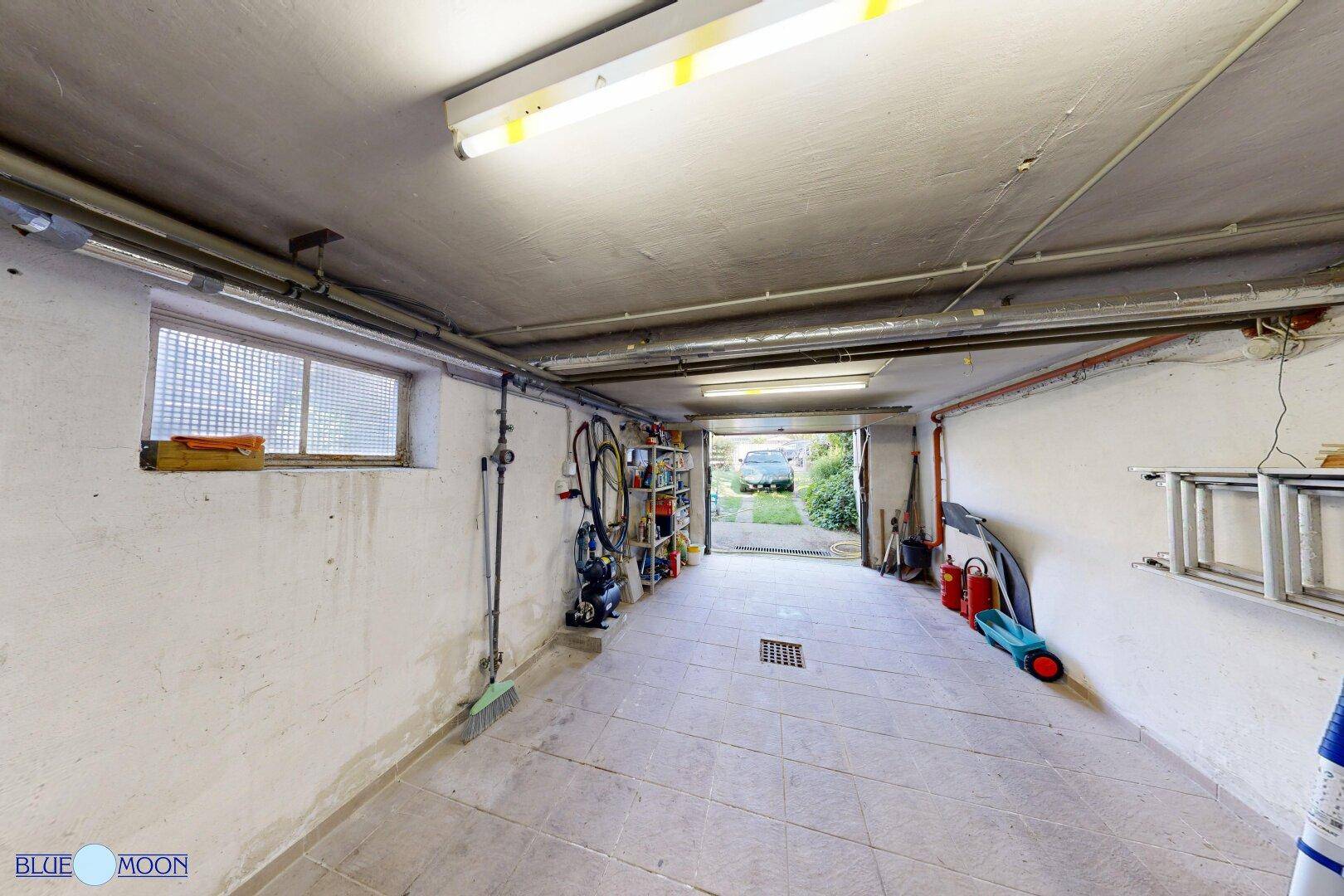 Geräumige Garage mit Fliesenboden, einem Fenster und Blick auf die Einfahrt im Freien.
