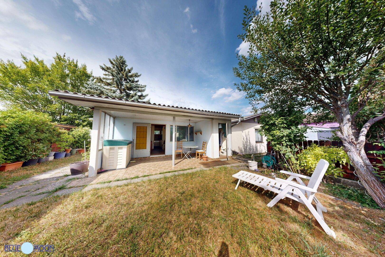 Überdachte Terrasse mit Sitzgelegenheiten und angrenzendem Gartenbereich mit Liegestuhl.