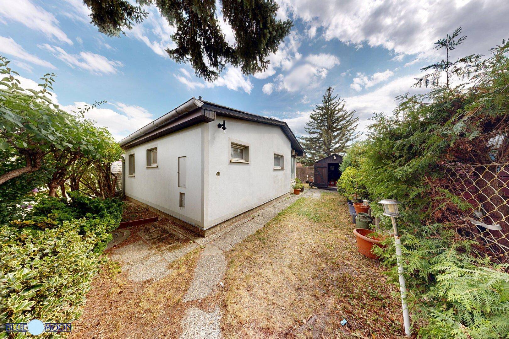 Seitenansicht des Hauses mit einem Gartenweg und einem kleinen Geräteschuppen im Grünen.
