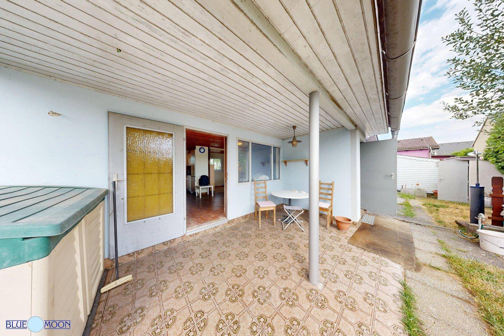 Überdachte Terrasse mit gemusterten Fliesen, kleinem Tisch und Stühlen, ideal für Mahlzeiten im Freien.