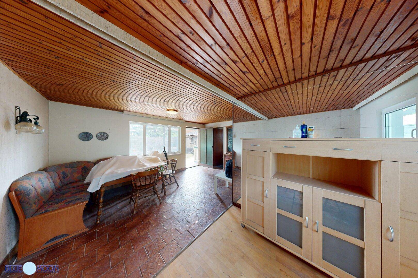 Heller Wohn-Essbereich mit Holztäfelung an der Decke und einem großen Holzschrank.