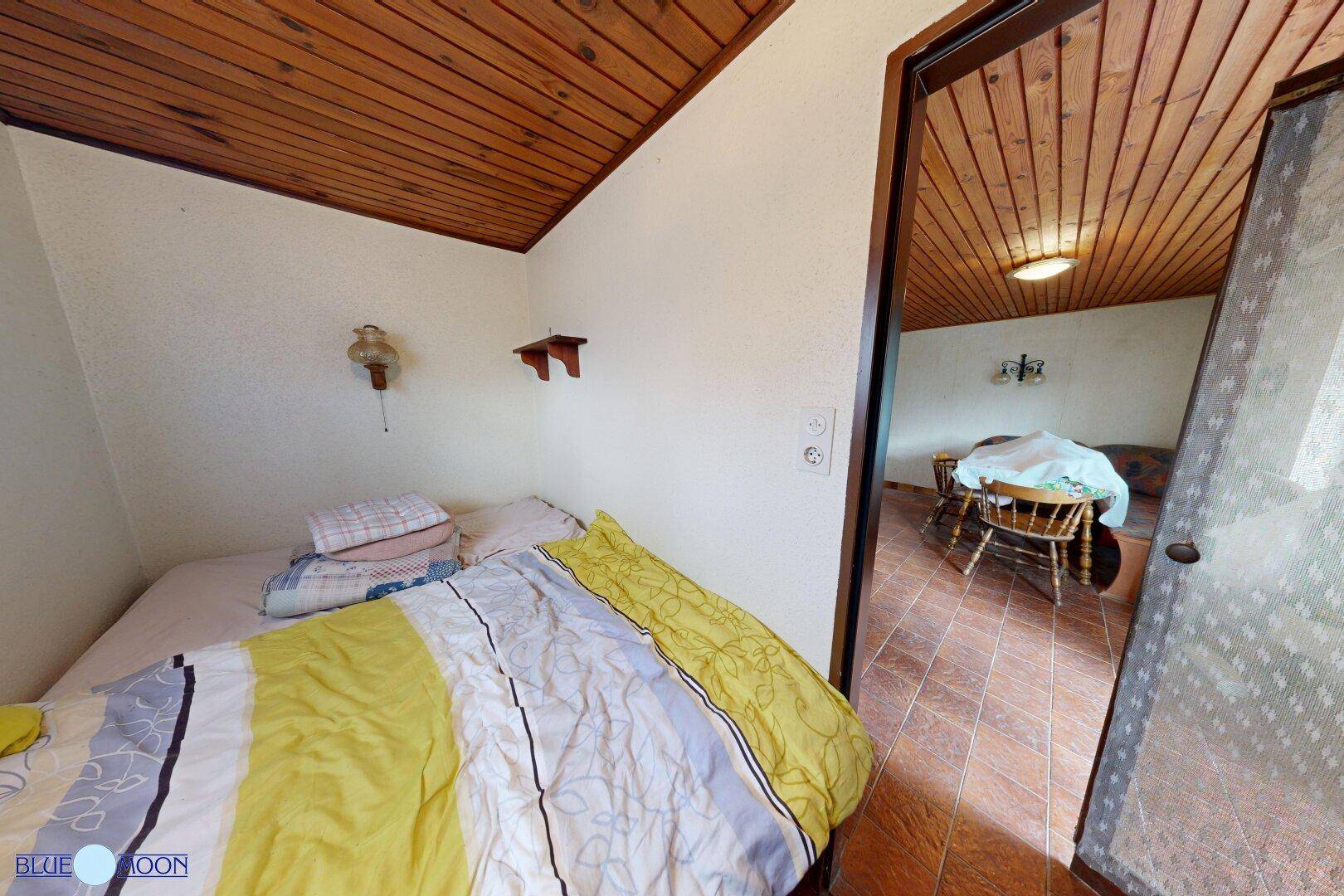 Kleines Schlafzimmer mit Einzelbett und Holztäfelung an der Decke, angrenzend an den Wohnbereich.