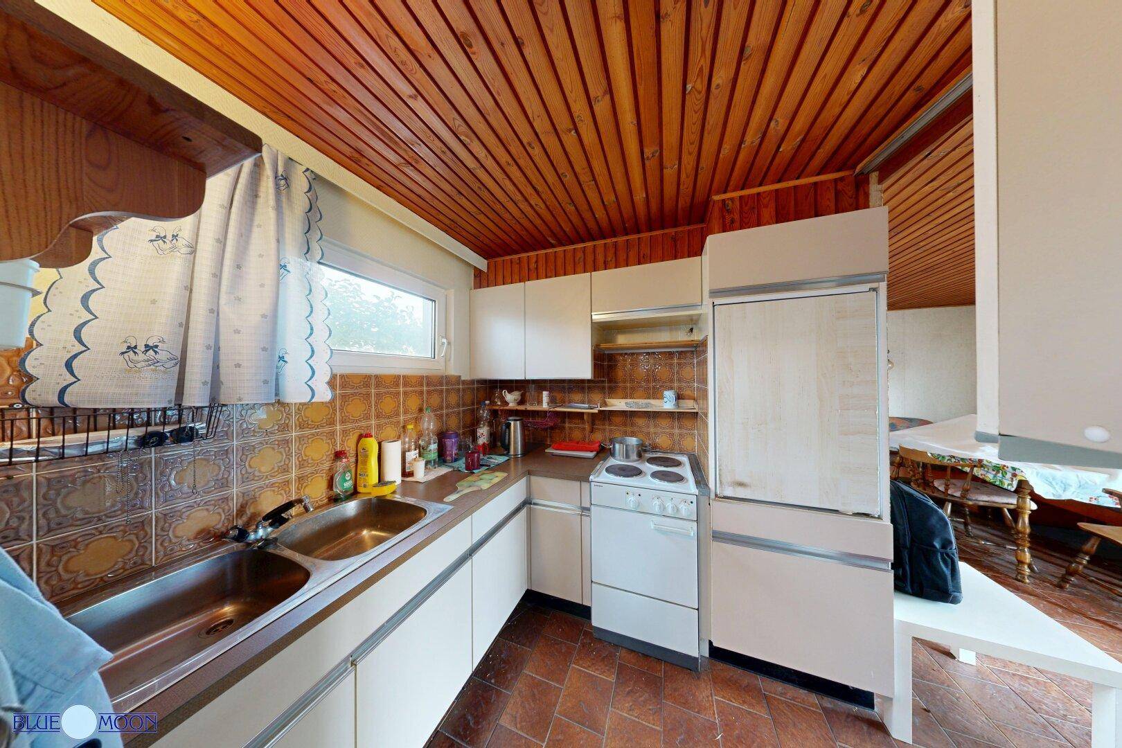 Funktionale Küche mit Fliesenboden, Holzdecke und einfachen Einbauschränken.
