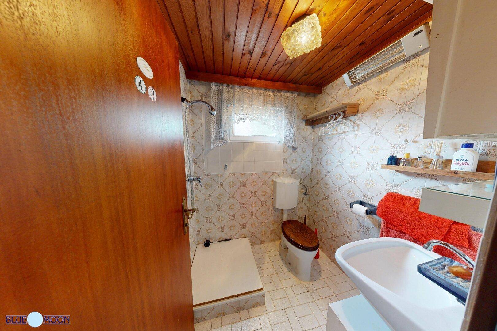 Kleines Badezimmer mit Dusche, WC und gemusterten Fliesen an Wänden und Boden.