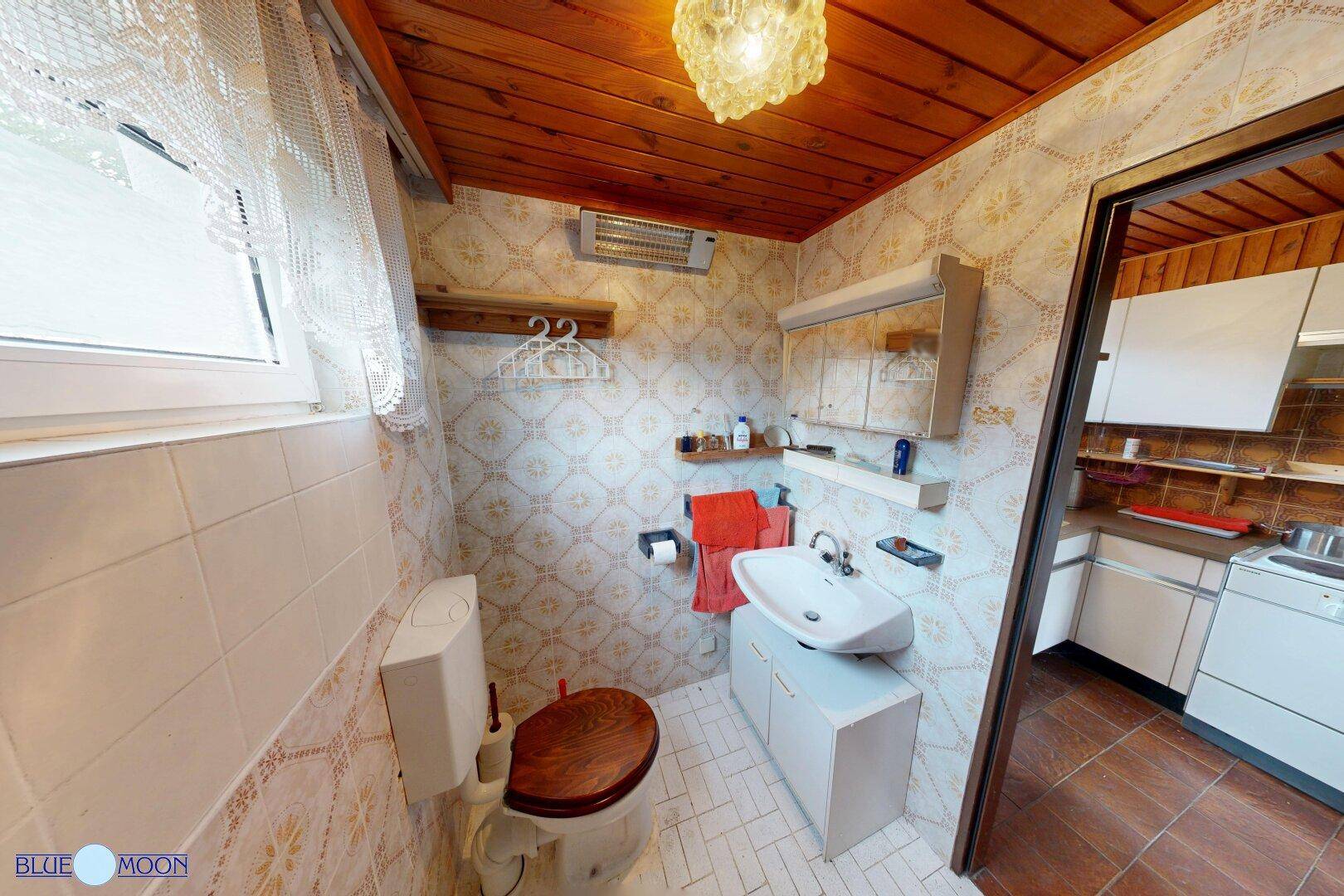 Badezimmer mit Waschbecken, WC und einem Spiegelschrank, durch eine Tür mit der Küche verbunden.