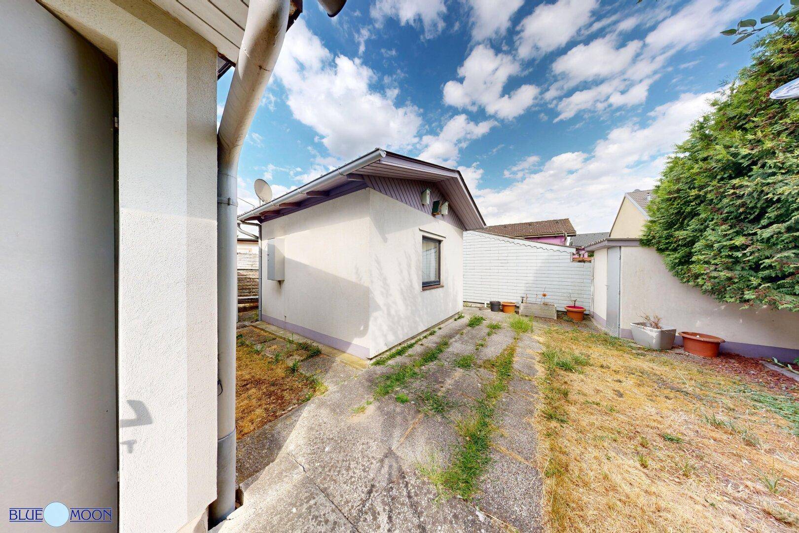 Seitenansicht eines kleinen Hauses mit weißer Fassade und einem gepflasterten Weg.