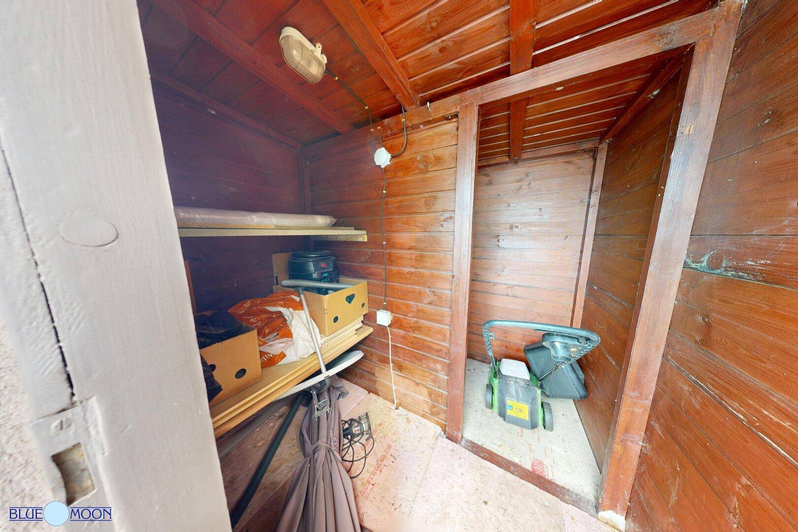 Innenansicht eines Holzschuppens mit Regalen und Stauraum für Gartengeräte.