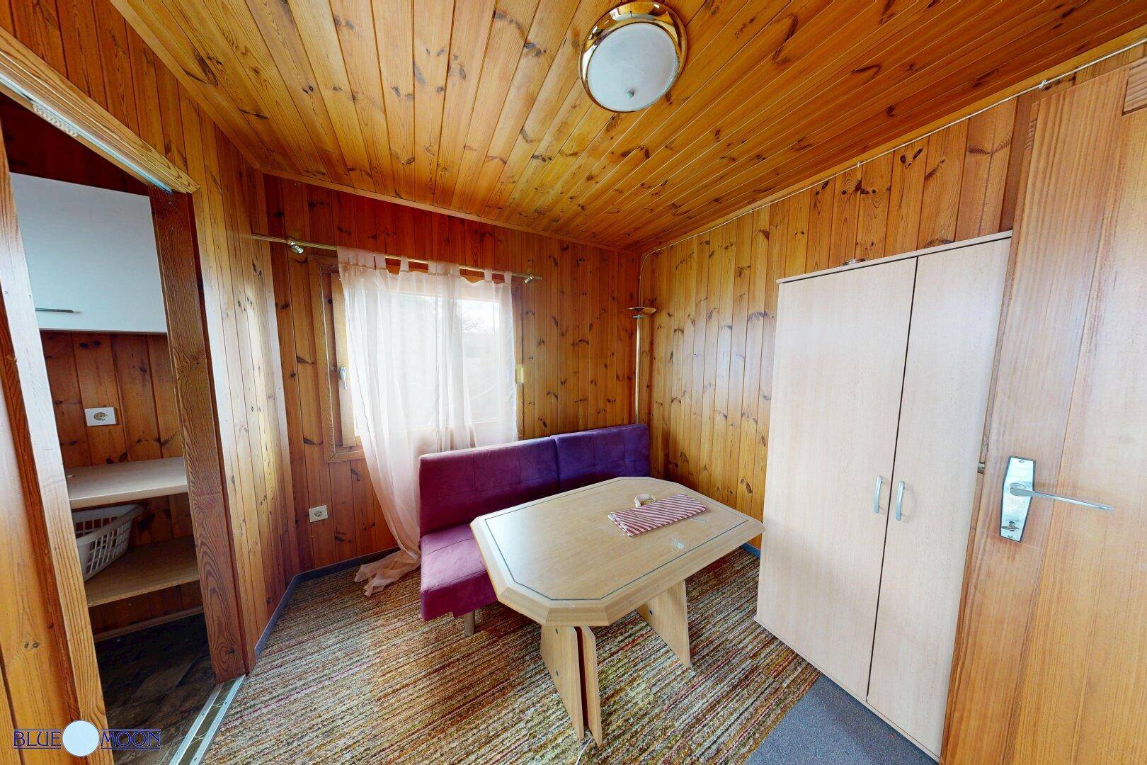 Gemütlicher Wohn-Essbereich in einem Holzhaus mit Holztäfelung und einfacher Einrichtung.