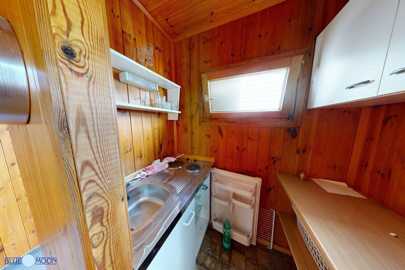 Kleine Küchenzeile in einem Holzhaus mit Spüle, Kochfeld und Kühlschrank.
