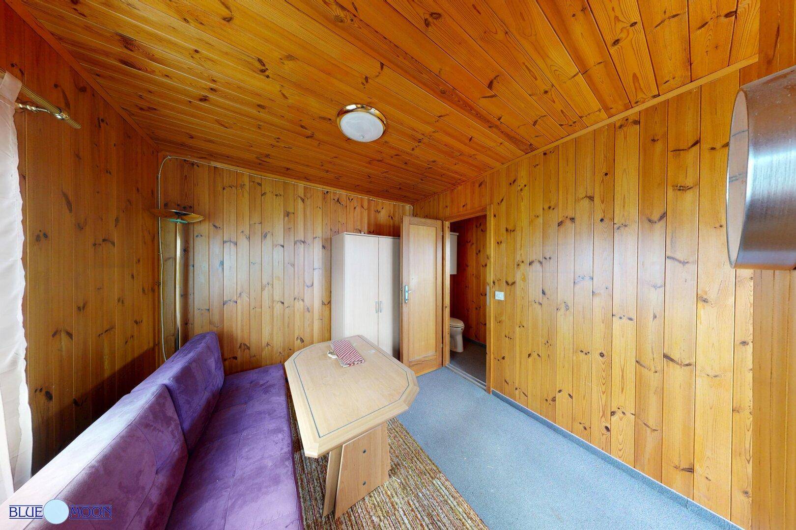 Wohn-Essbereich mit Holztäfelung, Sofa und Esstisch, ideal für ein kleines Ferienhaus.