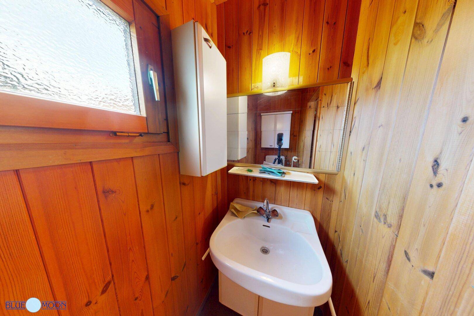Kleines Badezimmer in einem Holzhaus mit Waschbecken und Spiegelschrank.