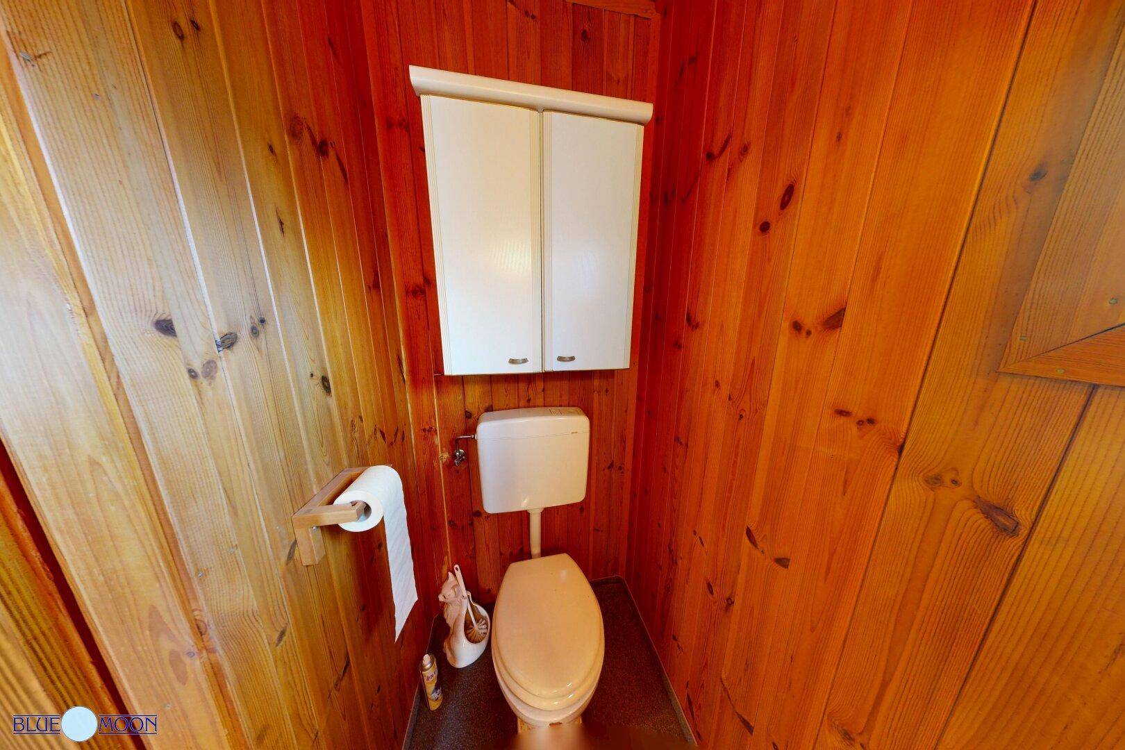 Separate Toilette in einem Holzhaus mit Holztäfelung an Wänden und Decke.