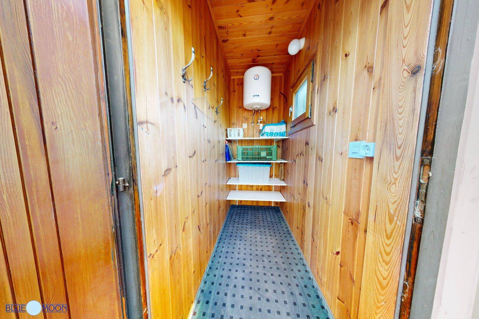 Schmaler Abstellraum mit Holzverkleidung, Warmwasserbereiter und praktischen Regalen für Lagerung.
