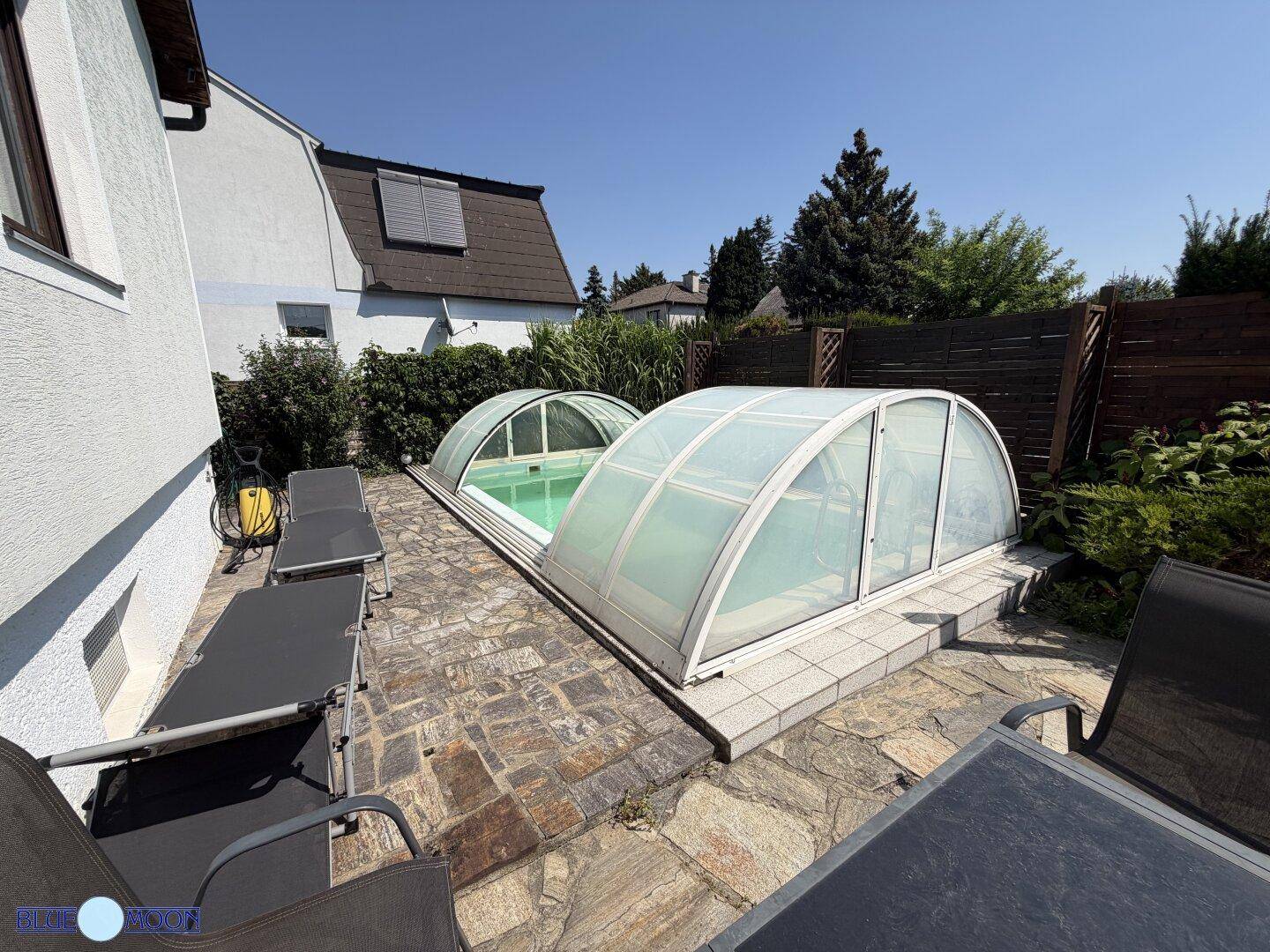 Geräumige Terrasse mit einem überdachten Pool, umgeben von Liegestühlen und Gartenmöbeln unter blauem Himmel.