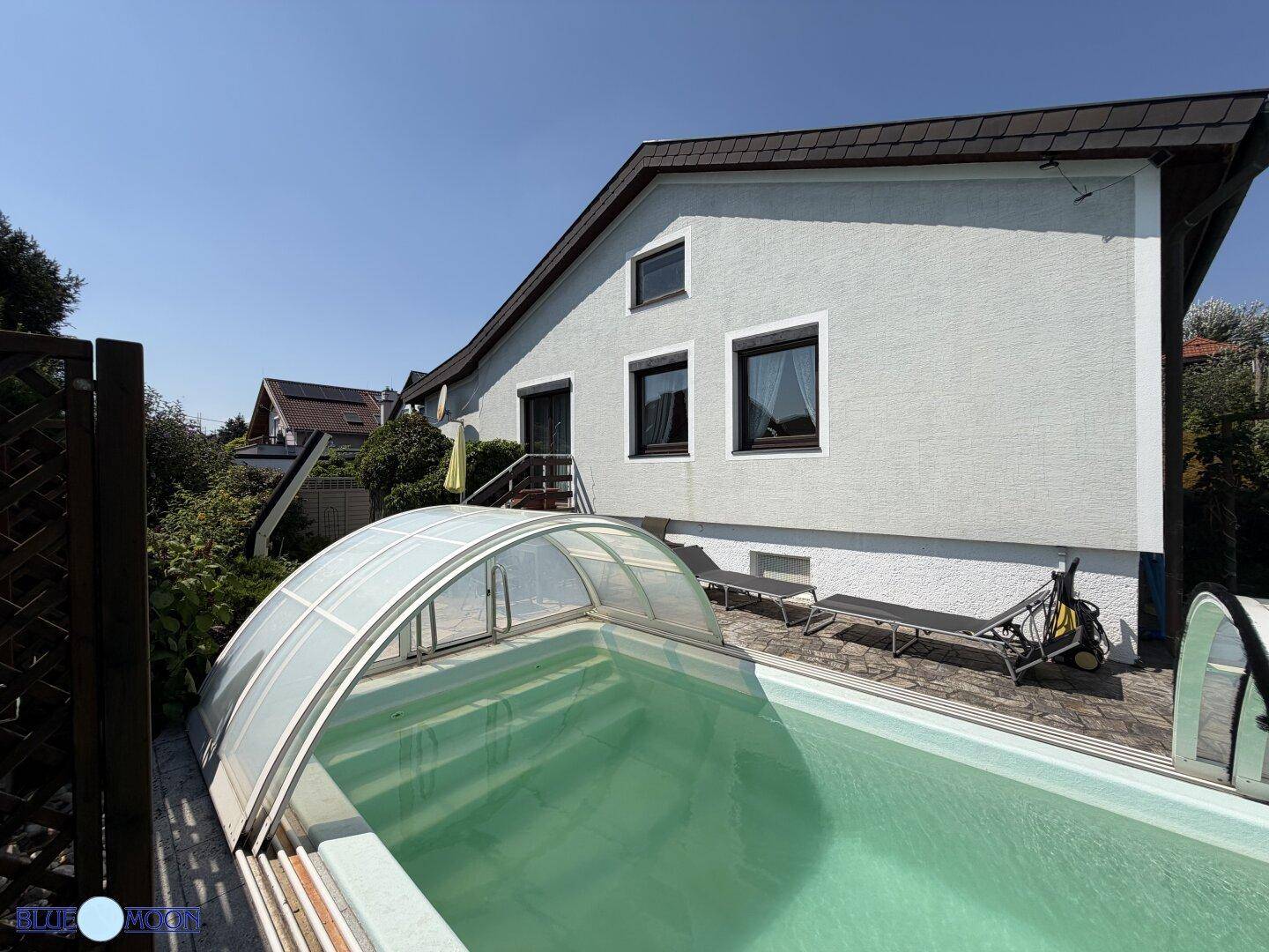 Ansicht der Hausfassade vom Poolbereich aus, mit Fenstern und einem sonnigen Außenbereich.