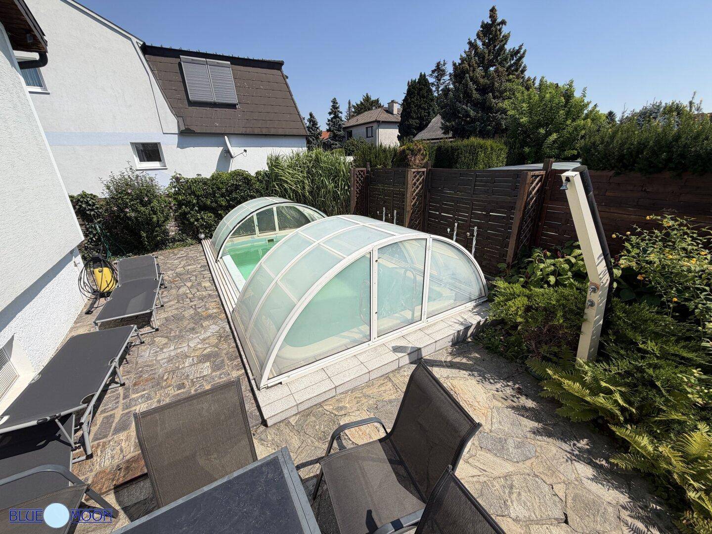 Weitläufige Steinterrasse mit einem überdachten Swimmingpool, Liegestühlen und einer praktischen Außendusche.