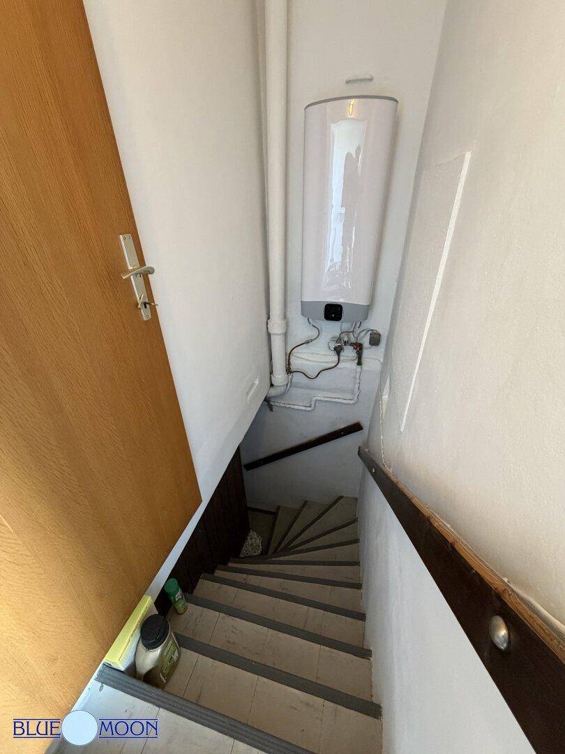 Treppe führt hinunter in den Kellerbereich, wo ein Warmwasserbereiter an der Wand montiert ist.