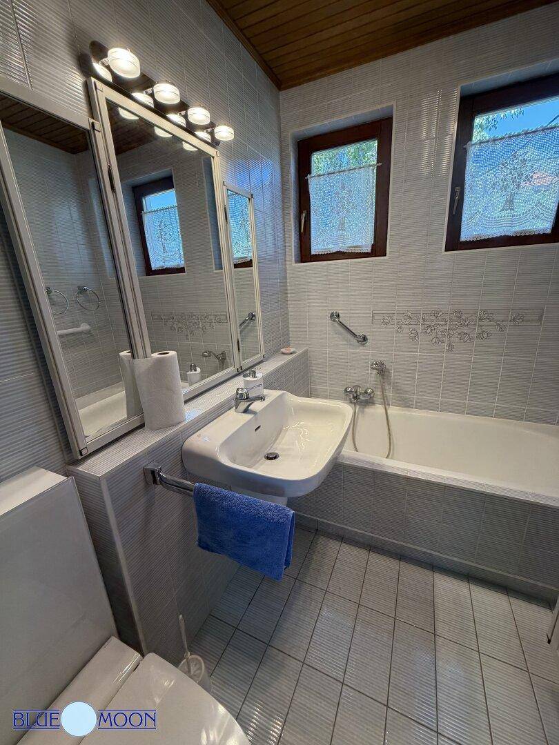 Helles Badezimmer mit Badewanne, Waschbecken, Spiegelschrank und hellen Fliesen an Wänden und Boden.