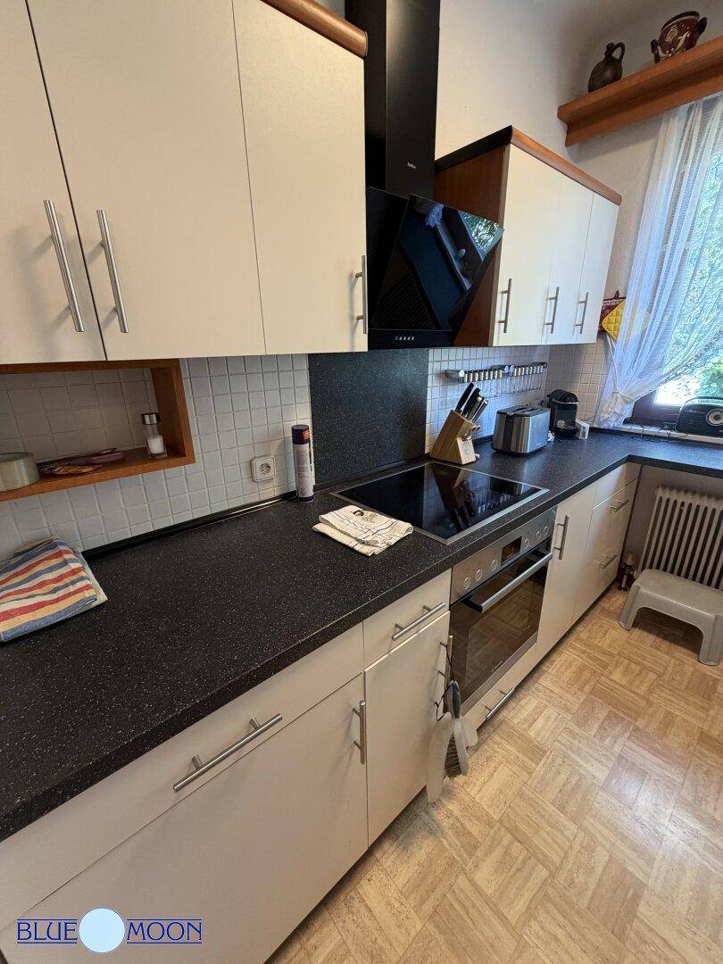 Moderne Küche mit weißen Schränken, schwarzer Arbeitsplatte, integriertem Backofen und Induktionskochfeld.