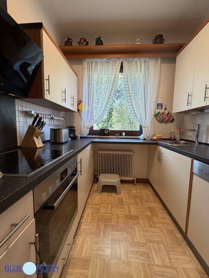 Funktionale Küche mit weißen Oberschränken, schwarzer Arbeitsplatte und einem Fenster mit Blick ins Grüne.