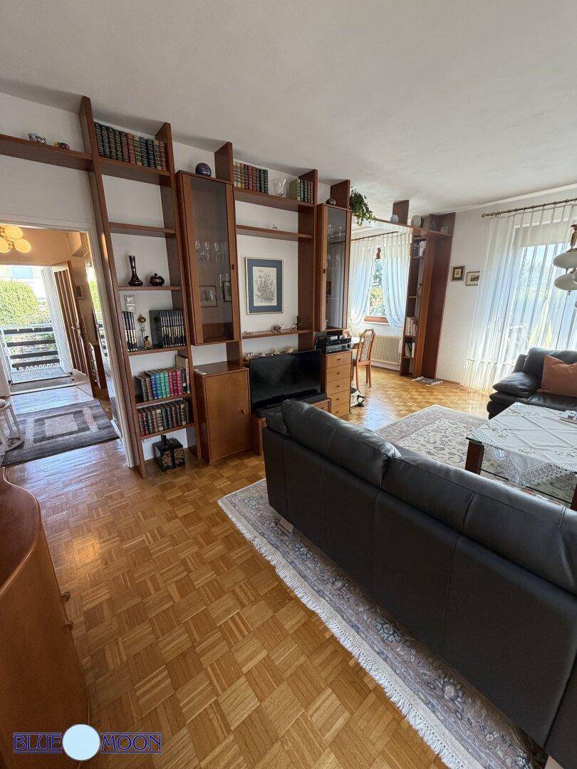 Geräumiges Wohnzimmer mit dunklen Ledersofas, Bücherregalen und Zugang zu einem Außenbereich.
