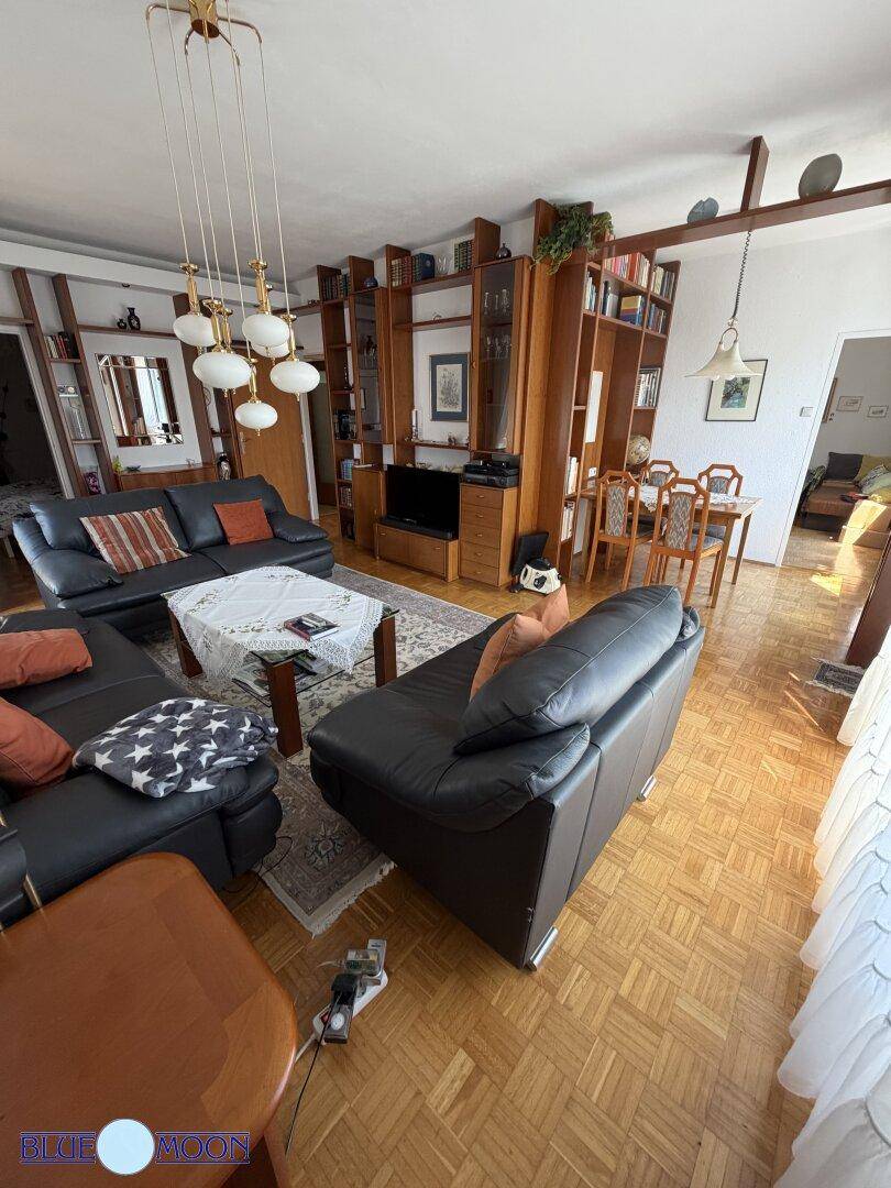 Wohn- und Essbereich mit Ledersitzgruppe, Holzwandregalen und einem Essbereich im Hintergrund.