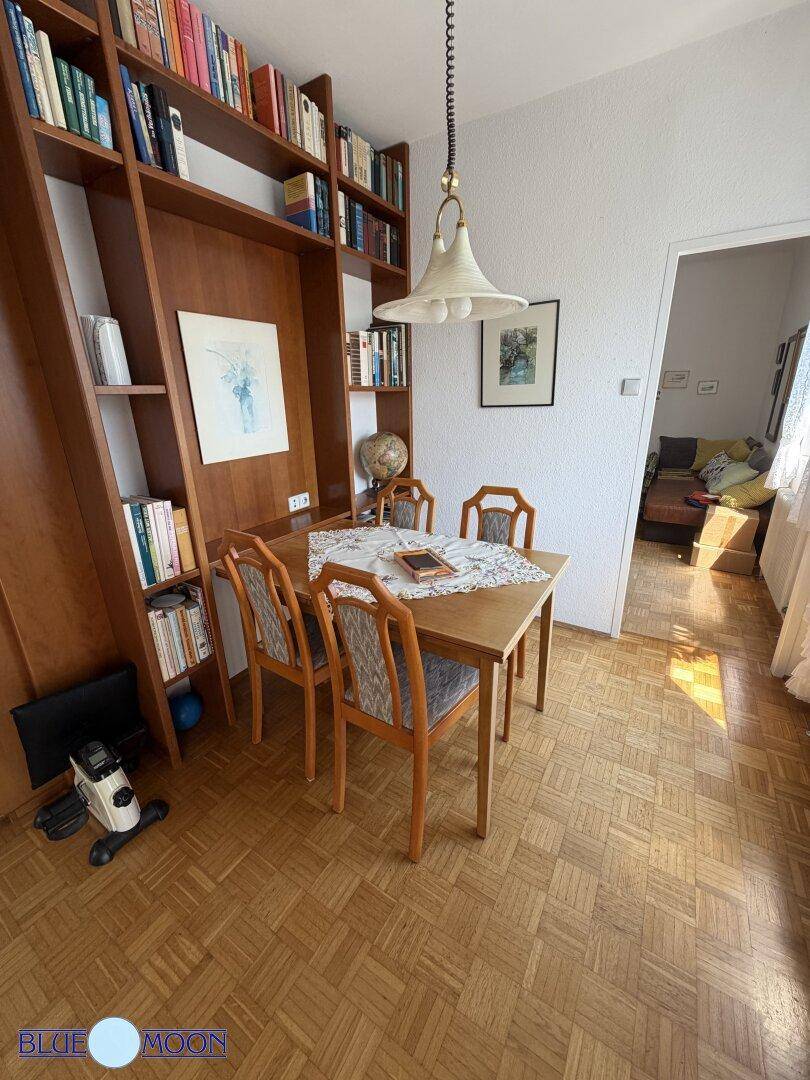 Essbereich mit Holztisch und Stühlen, umgeben von einem großen Bücherregal und Parkettboden.