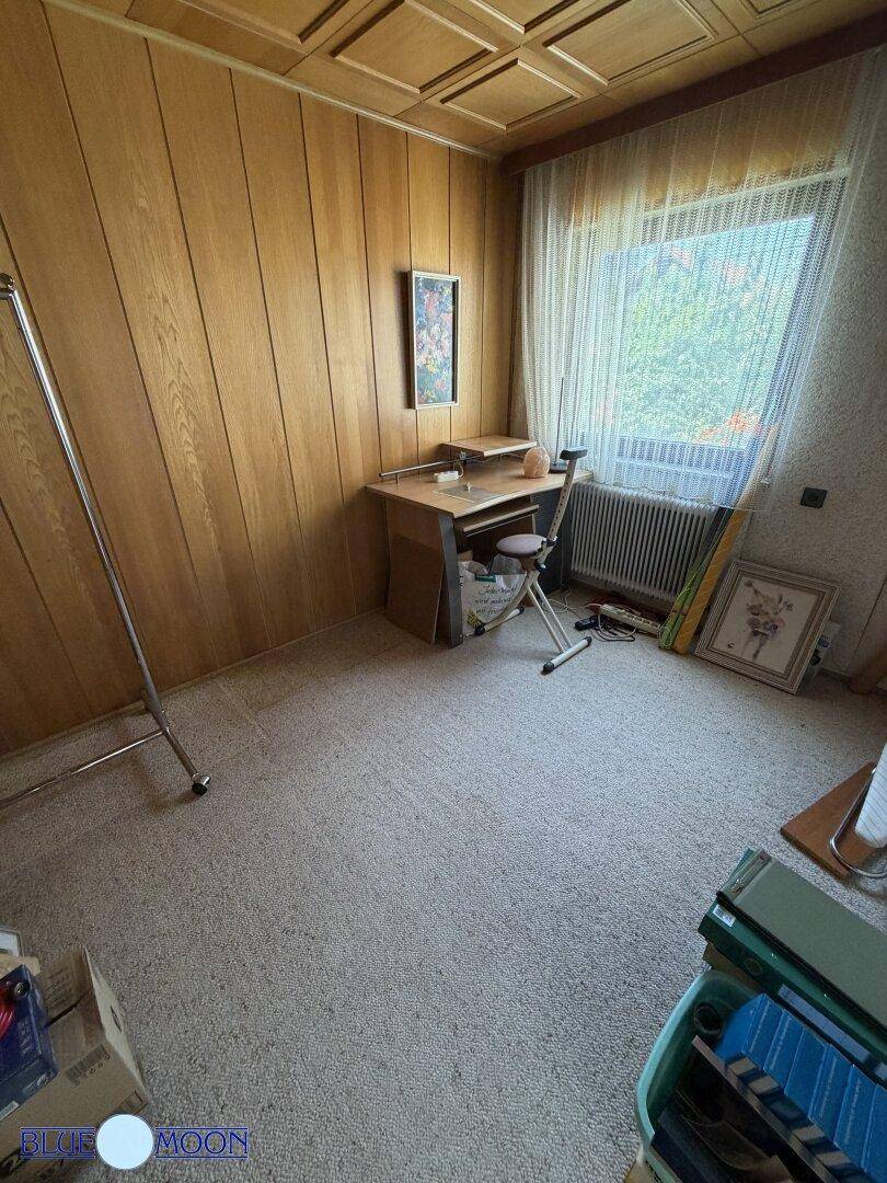 Zimmer mit Holzvertäfelung, Teppichboden und einem Schreibtisch, ideal als Arbeitszimmer nutzbar.