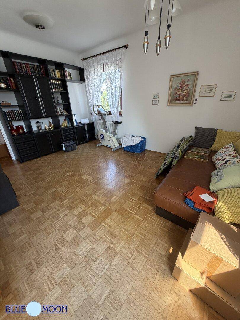 Vielseitiger Raum mit Parkettboden, Sofa und einem Heimtrainer, nutzbar als Hobby- oder Wohnzimmer.