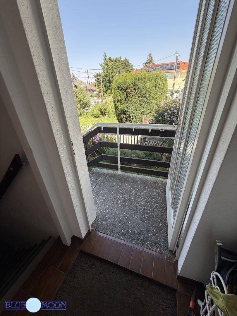 Kleiner Balkon mit Betonboden und Holzgeländer, bietet einen Blick ins Grüne.